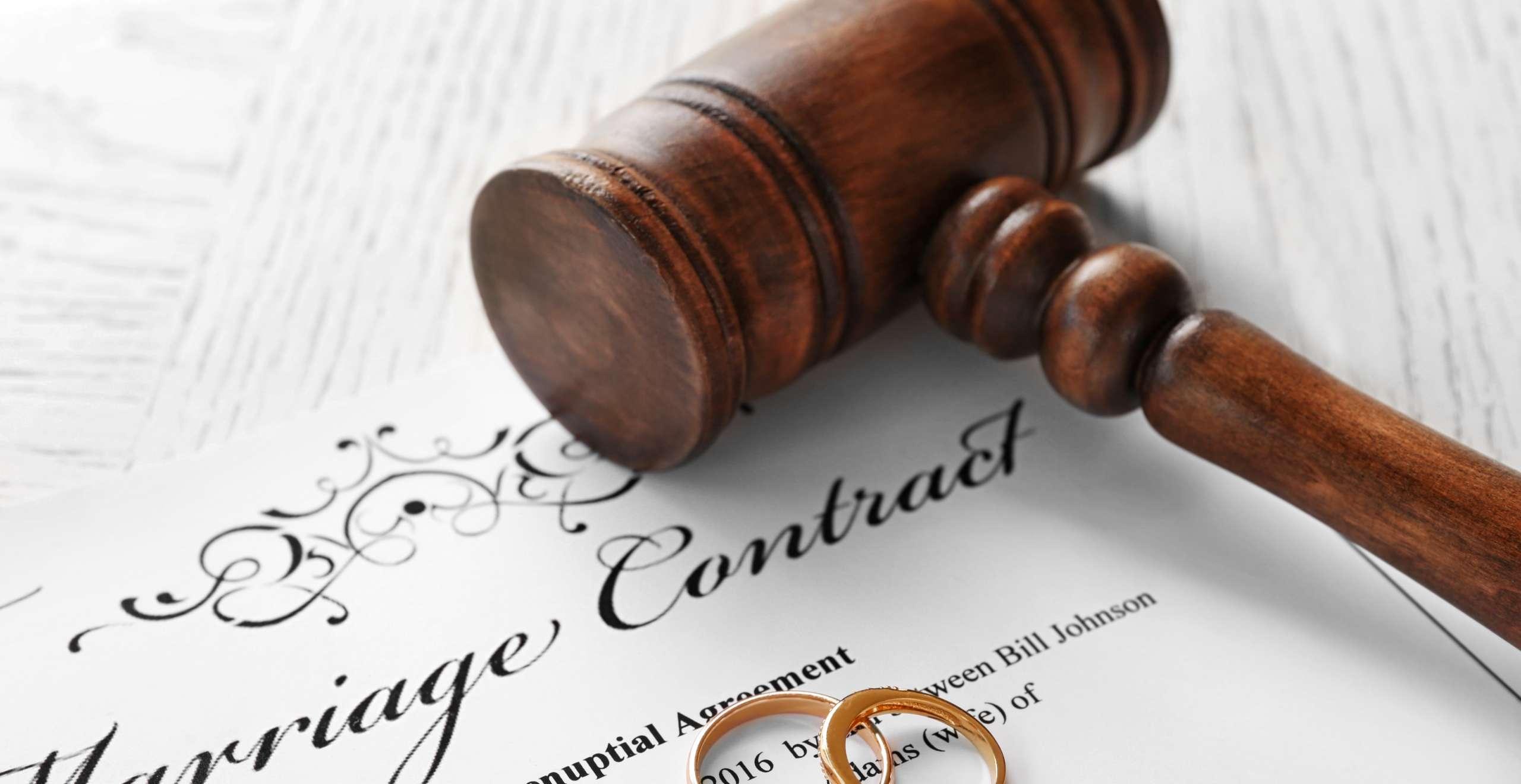 Golden wedding rings with judge gavel on marriage contract, closeup